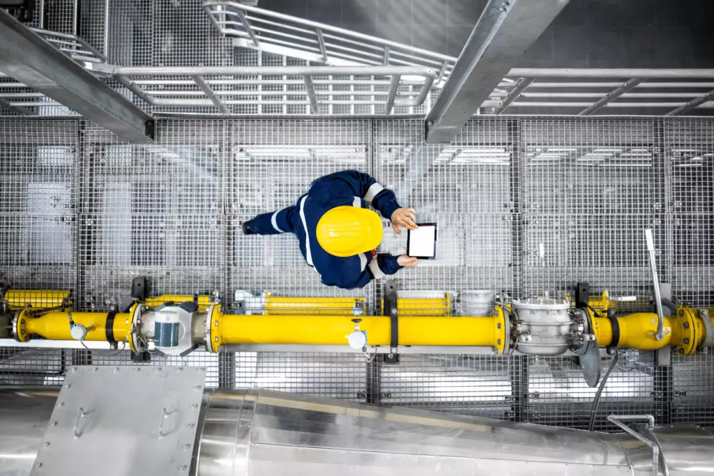 Vue de dessus d'un ouvrier de la raffinerie marchant près des conduites de gaz, vérifiant l'approvisionnement en essence et les installations dans l'usine de production. - Yélé Consulting