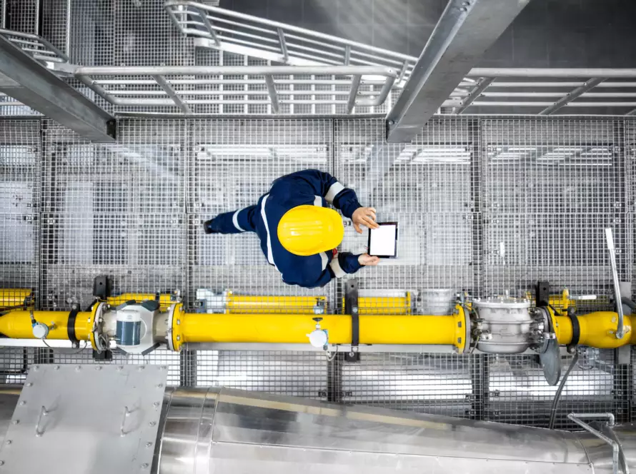 Vue de dessus d'un ouvrier de la raffinerie marchant près des conduites de gaz, vérifiant l'approvisionnement en essence et les installations dans l'usine de production. - Yélé Consulting